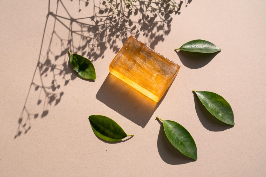 pexels photo 7615806 7615806 Flat lay of a natural soap bar with green leaves and shadows on a beige surface.